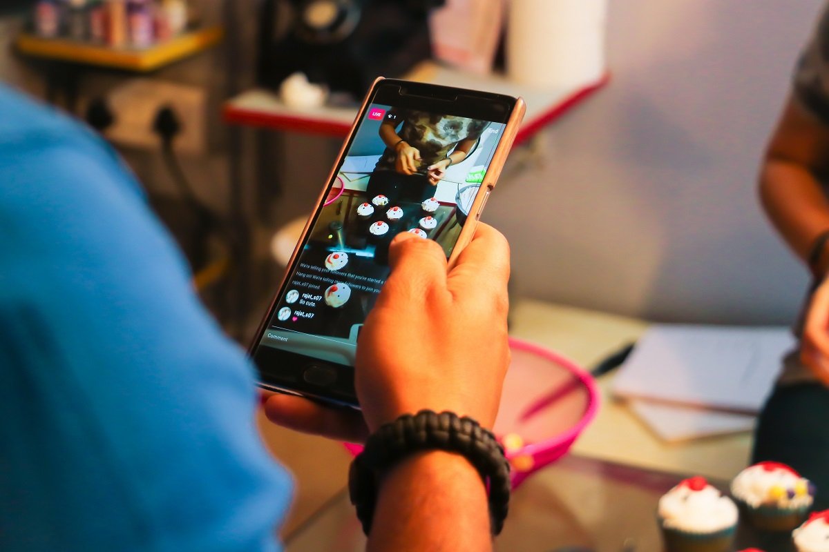 A hand holding a phone displaying a social media video from a bakery with multiple cupcakes on a table.