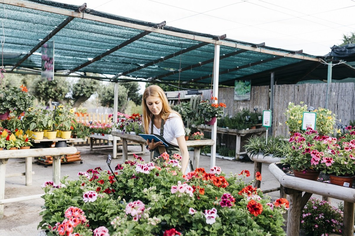 A woman holding a tablet and looking at flowers.