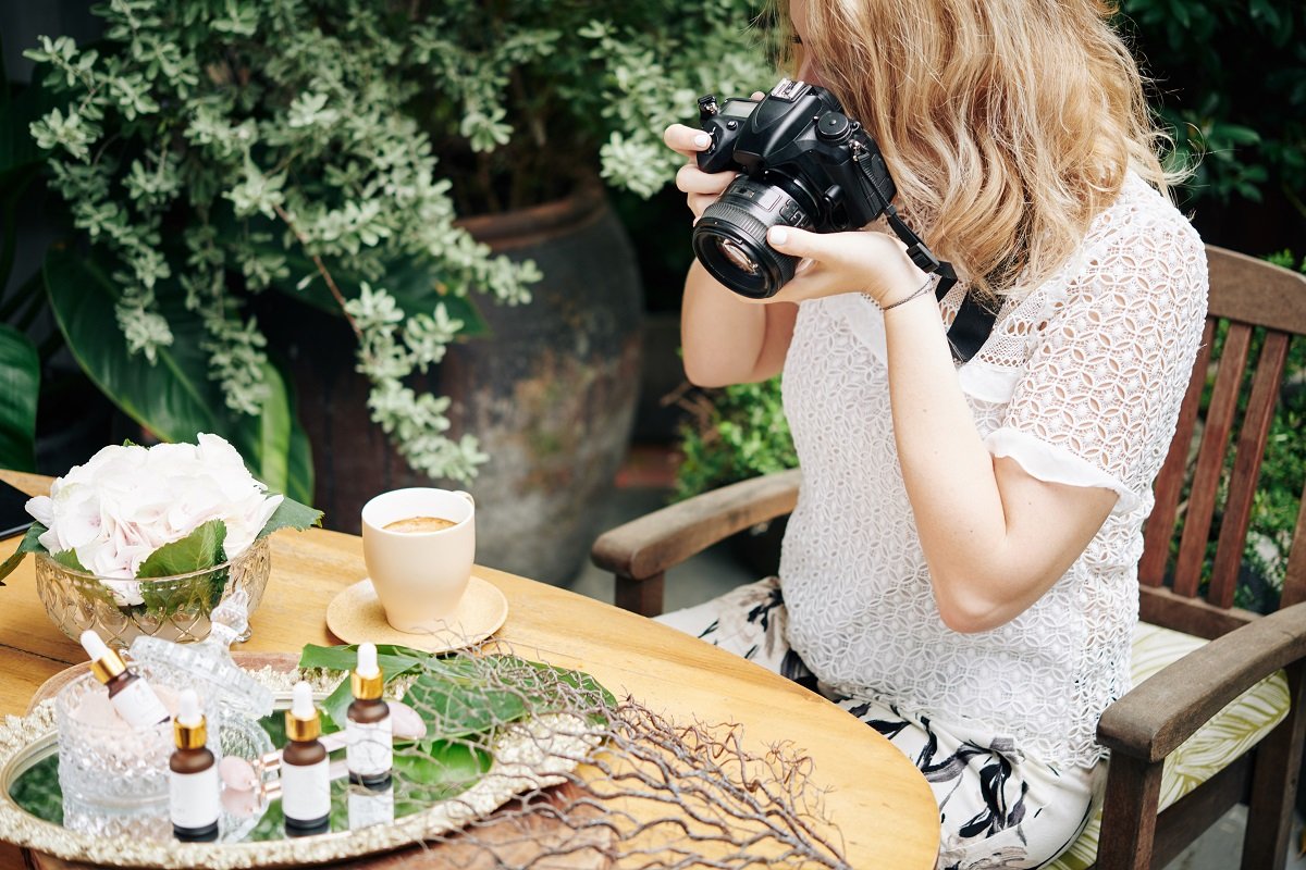 A photographer taking a picture of unbranded cosmetics on an outdoor table
