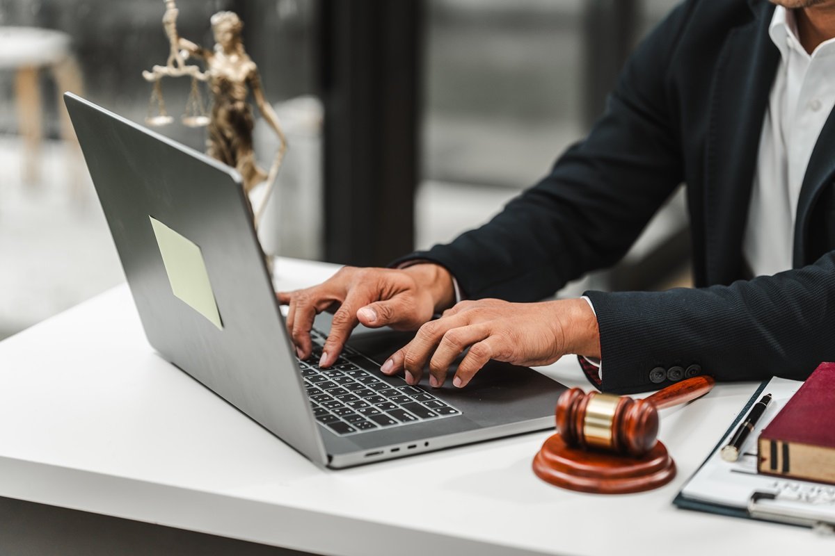 A lawyer using a laptop next to a gavel and statue of Lady Justice