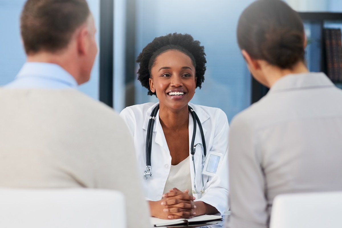 A female doctor speaking with one male and one female patient